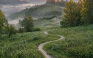 A dirt path through green hills in morning mist.