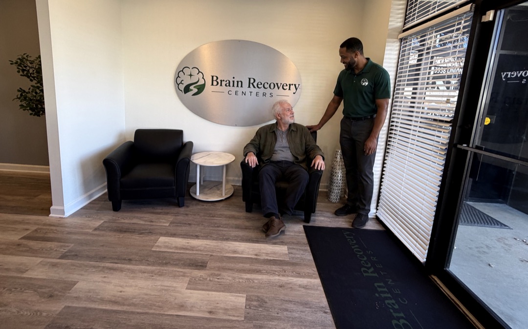 The lobby of our South County clinic: under the Brain Recovery Centers sign, a staff member in a Brain Recovery Centers polo talks with a seated visitor.