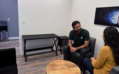 A staff member in a Brain Recovery Centers polo and a visitor talk in a consult room.