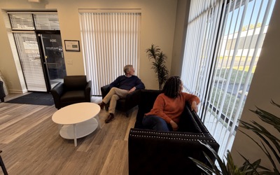 Two visitors talk in the lounge by the front windows.