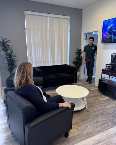 A visitor waits in the lounge while a staff member in a Brain Recovery Centers polo comes through the door.