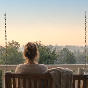 A woman sitting on a porch swing at dawn.