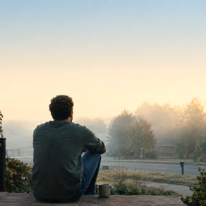 A man sitting on porch steps with a coffee mug at dawn.