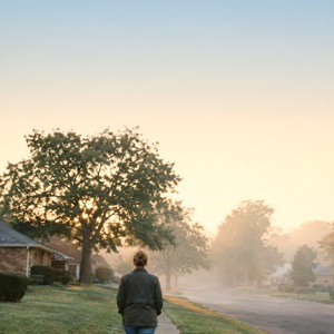 A man in a jacket walking down a misty street.